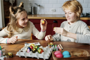 2 kids in beige decorating easter eggs